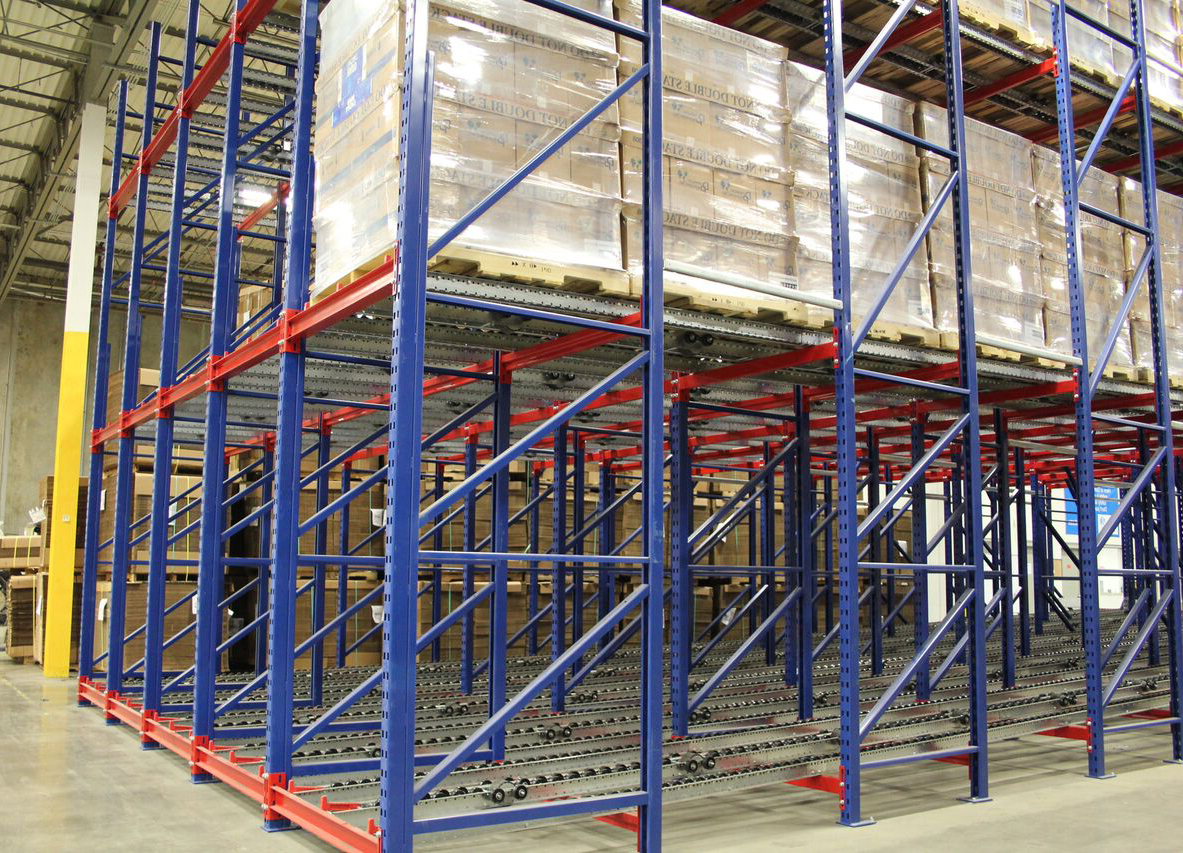 Tall pallet flow racking with blue frames and orange beams, showing the gravity roller lanes at the base and wrapped pallets loaded above